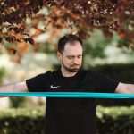 Man using resistance band for exercise in a sunny outdoor setting.